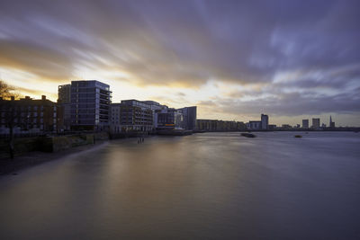 River by buildings against sky at sunset