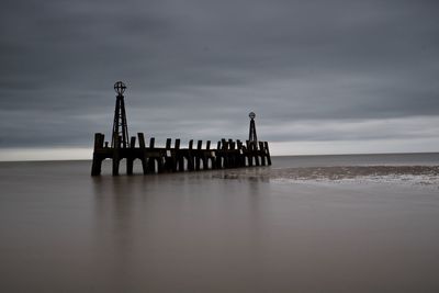 Silhouette wooden posts on beach against sky