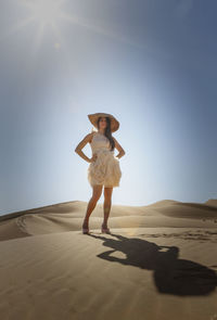 Full length of woman standing on sand dune against sky