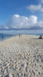 People at beach against cloudy sky during sunny day