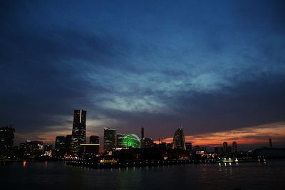 Illuminated city at waterfront during sunset