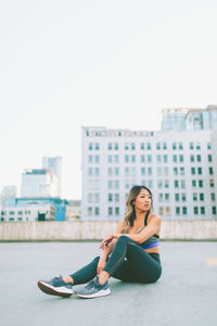 Young woman sitting in city against sky