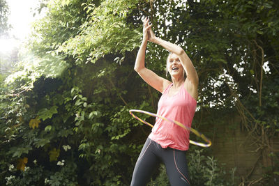 Active senior spinning hula hoop while standing in back yard on sunny day