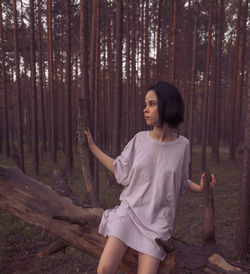 Young woman standing by tree trunk in forest