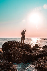 Man standing on rock at beach against sky during sunset