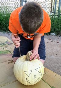 Full length of a boy carving a white pumpkin