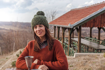 Smiling woman looking away with drink in container on table during winter