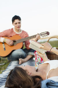 Teenage girl reading book with boyfriend playing guitar