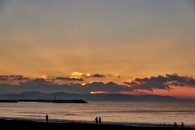 Scenic view of sea with silhouette people against sky during sunrise