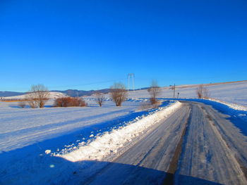 Snow covered road against clear blue sky