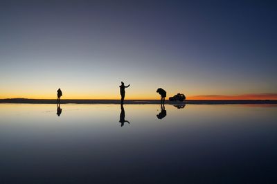 Silhouette people by lake against sky during sunset