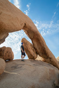 Wide angle view of man looking at arch rock in joshua tree national park against clear sky.