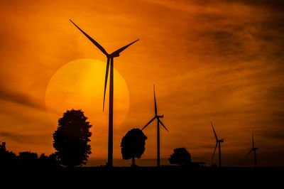 Silhouette wind turbines on field against orange sky