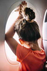 Rear view of girl looking through airplane window