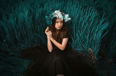 Portrait of woman wearing flowers while sitting against plants