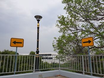 Road sign by trees against sky