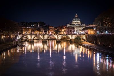 Illuminated bridge over river by buildings against sky at night