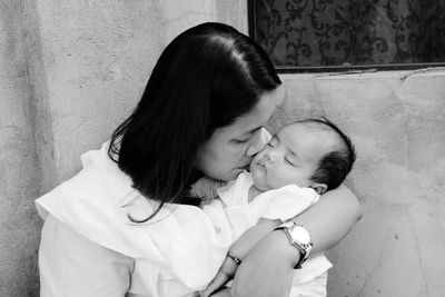 Mother kissing baby while sitting against wall