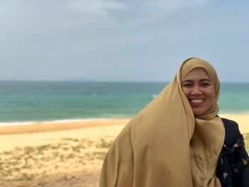 Portrait of smiling mature woman wearing hijab against sea at beach