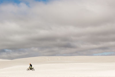 Man riding motorcycle on sand against cloudy sky
