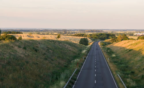 Empty road amidst field against sky