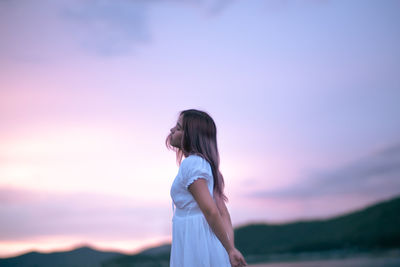 Side view of woman standing against sky during sunset