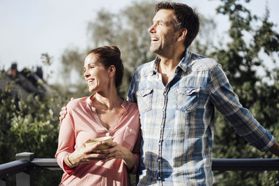 Happy friends with arms raised against trees