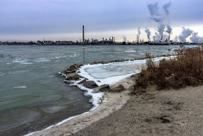 Smoke emitting from factory by sea against sky