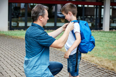 Dad, dad puts a blue backpack on his son. parents accompany their children to school. back to school
