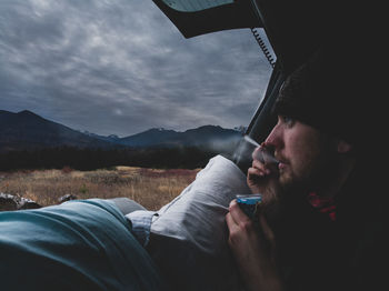 Portrait of young man holding mountains against sky