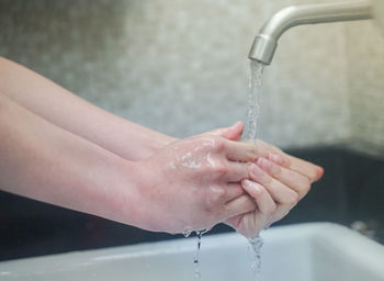Close-up of hand touching water from faucet in bathroom