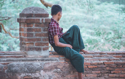 Side view of teenage girl sitting on stone wall