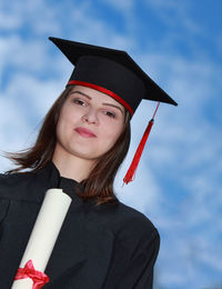 Portrait of young woman wearing mortarboard against sky