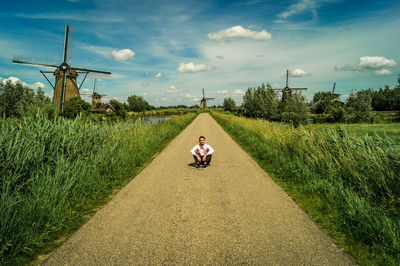 Portrait of man sitting on road amidst agricultural fields