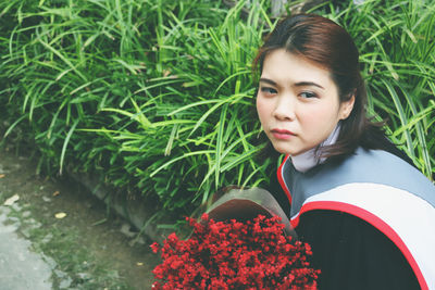 Young woman wearing graduation gown with bouquet