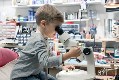 Boy using microscope while sitting on table