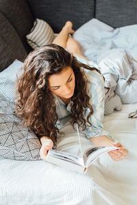 High angle view of young woman reading book while lying on bed at home