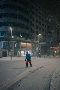 Anonymous male athlete in sportswear skiing on snowy road against building in evening during snowfall in madrid spain