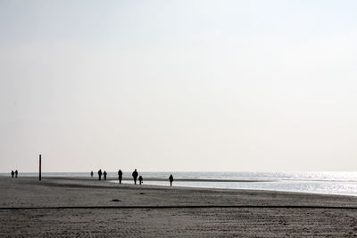 Silhouette people on beach against clear sky