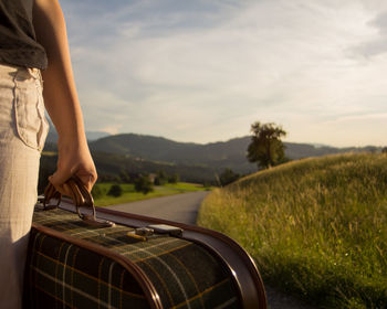 Midsection of woman holding suitcase on road against sky