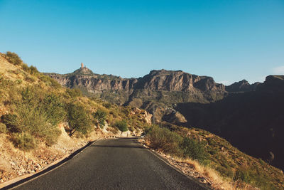 Road amidst mountains against clear blue sky