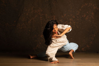 Young woman looking away while sitting on wooden floor