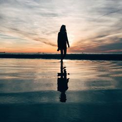 Rear view of silhouette woman standing at beach during sunset