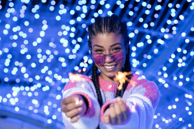 Cheerful black woman with braided hairstyle and pink glasses enjoying christmas lights