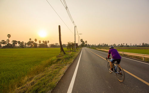 Rear view of woman riding bicycle on road against sky