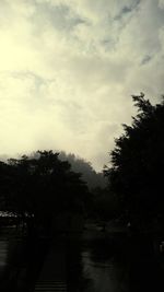 Silhouette trees by river against sky