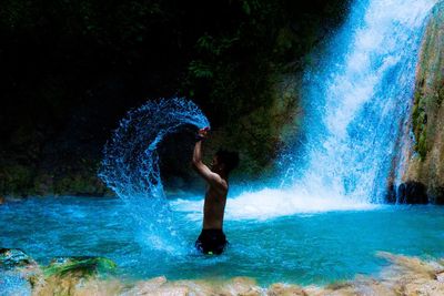 Side view of man splashing water by waterfall