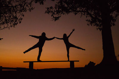 Silhouette man with arms outstretched against orange sky