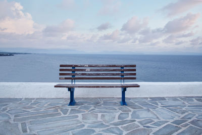 Empty bench on beach by sea against sky