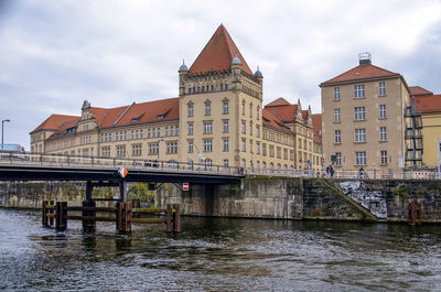 Bridge over river by buildings against sky